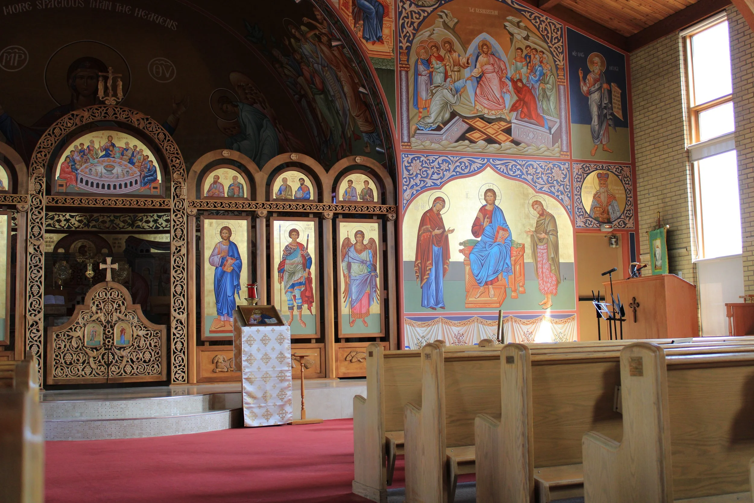 Interior of a church with religious paintings on the walls, wooden pews, and a red carpet leading to the altar.