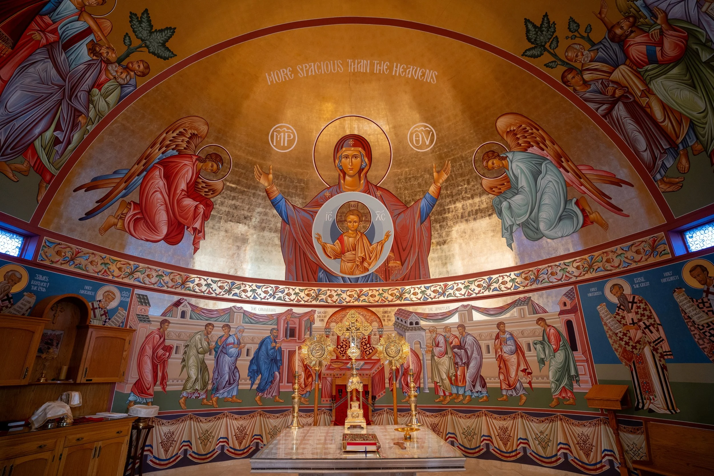 Christian altar inside a church with gold background, surrounded by religious paintings of angels and saints, with ornate coverings and religious items on the table.