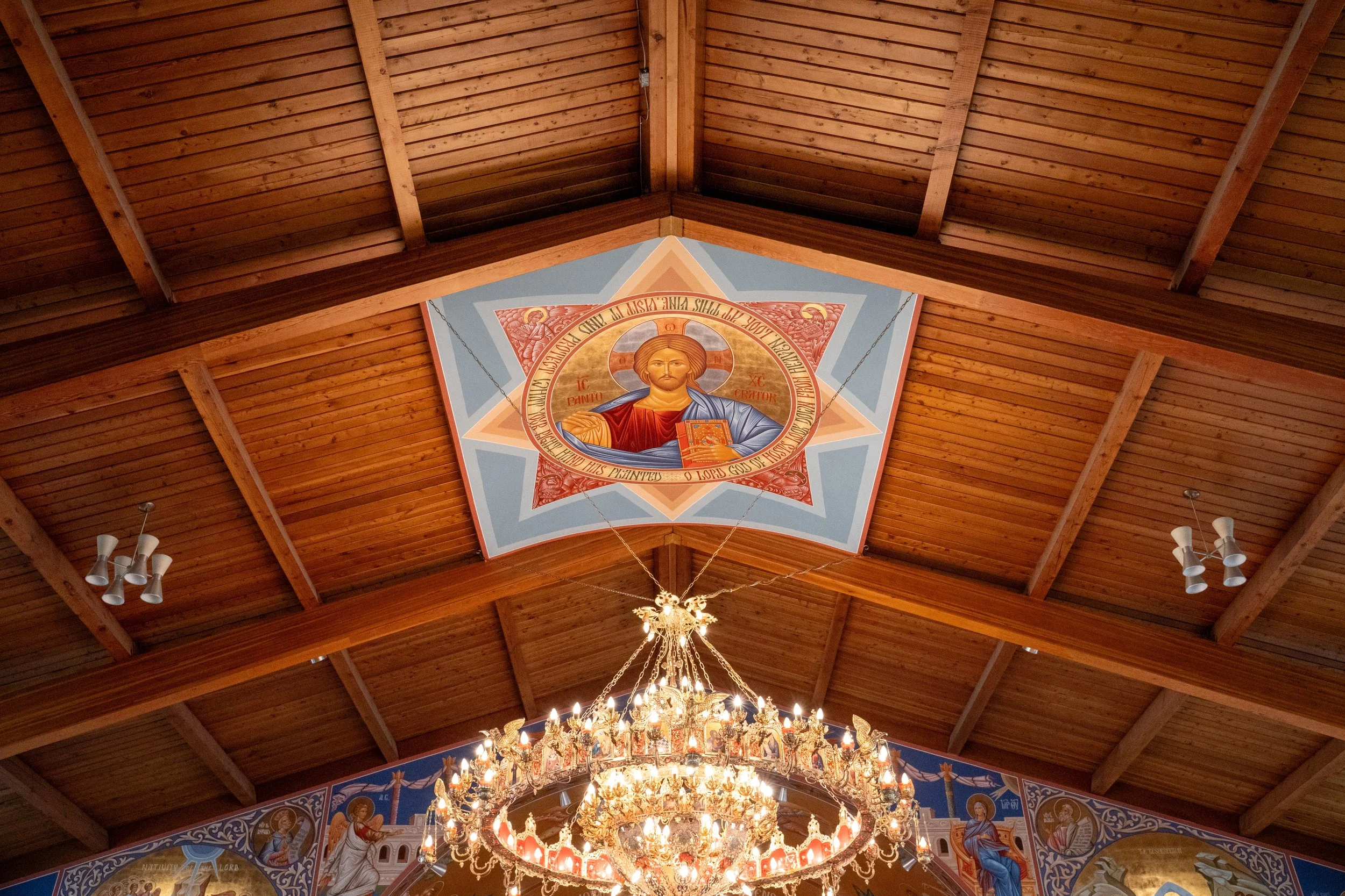 Interior view of a wooden church ceiling with religious iconography and a chandelier.