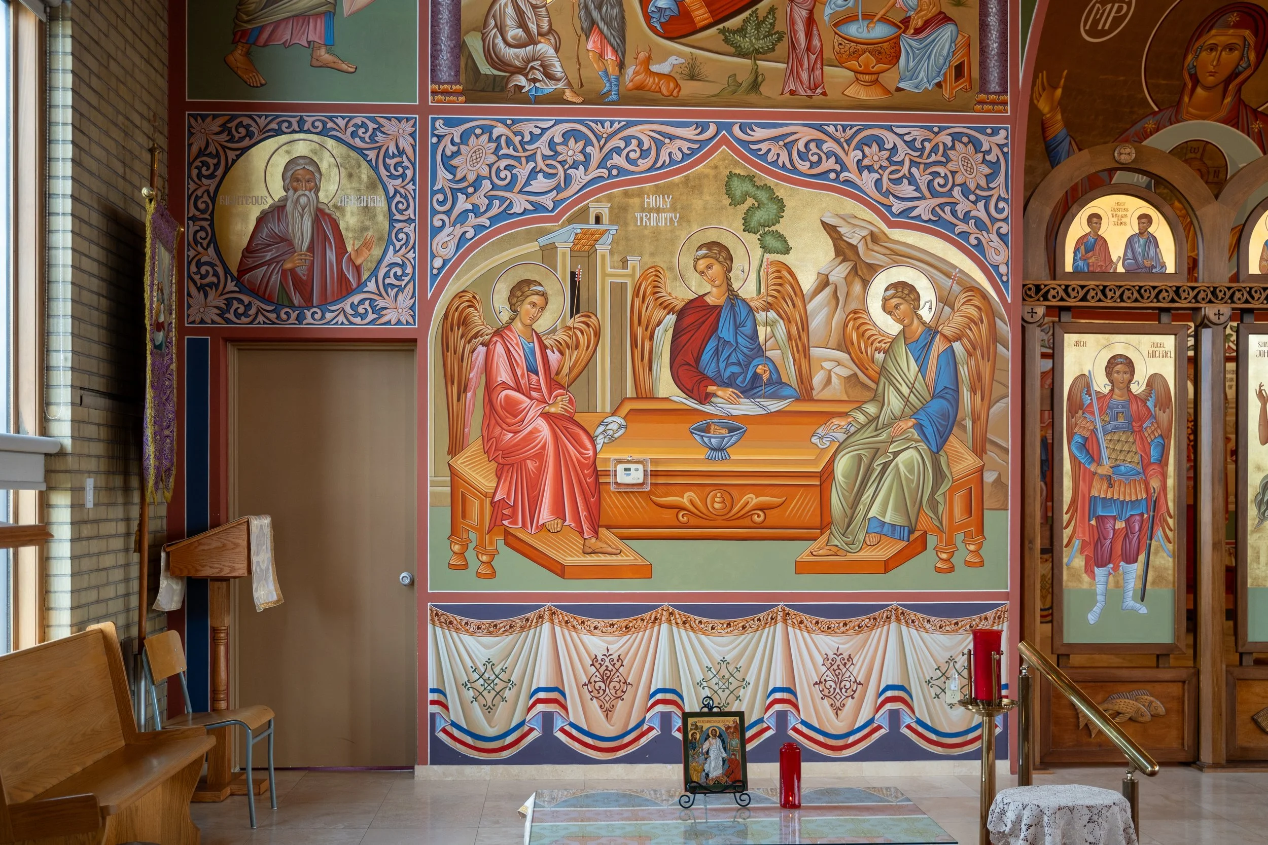 Colorful religious mural inside a church, depicting angels and saints, with intricate floral patterns and religious symbols.