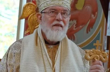 The Most Reverend Dr. Nathaniel (Popp) Archbishop of Detroit and the Romanian Orthodox Episcopate dressed in religious attire holding a staff, standing inside a church with religious decorations.