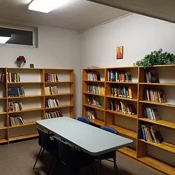 Saint George Orthodox Cathedral library room with wooden bookshelves filled with books, a table in the center, a small window, and a painting on the wall.