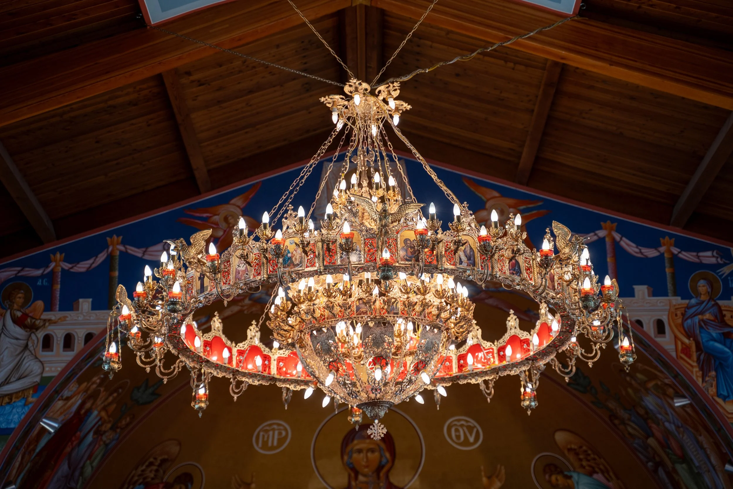 A large ornate chandelier hanging from a wooden cathedral ceiling with religious icons and images in the background.