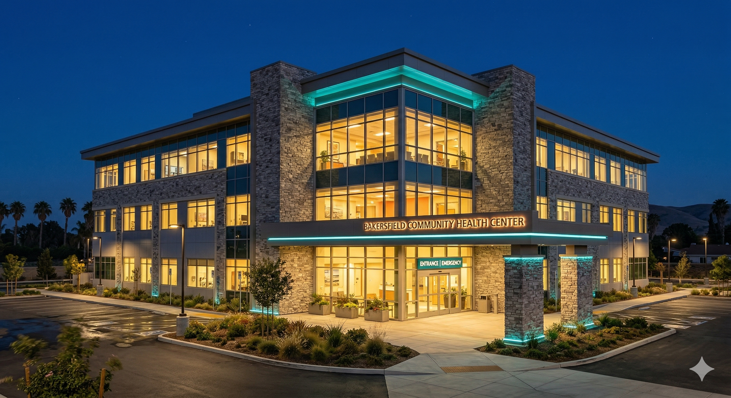 Exterior of Bakersfield Community Health Center at dusk with lit windows, parking lot, landscaped entrance, and illuminated signs for emergency and entrance.