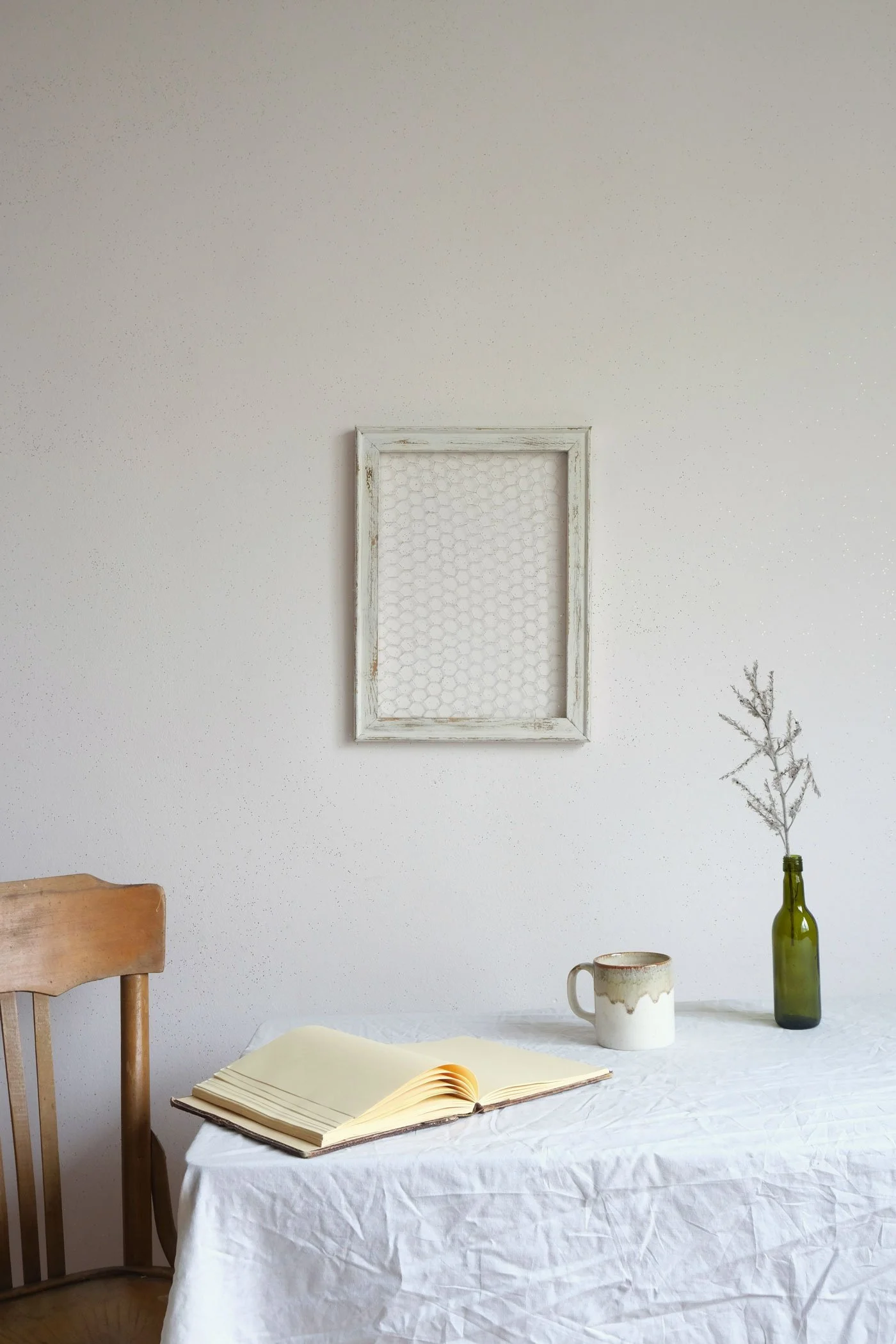Open journal and ceramic mug on a linen-covered table beside a wooden chair in a calm minimal space, representing a life coaching session