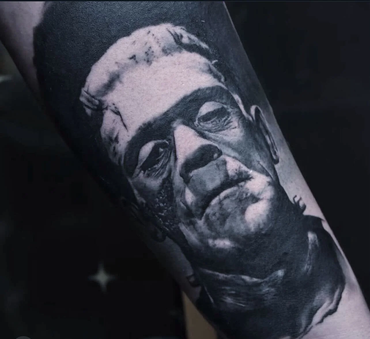 Black and gray realistic portrait of a man with glasses and short hair tattooed on a person's arm.