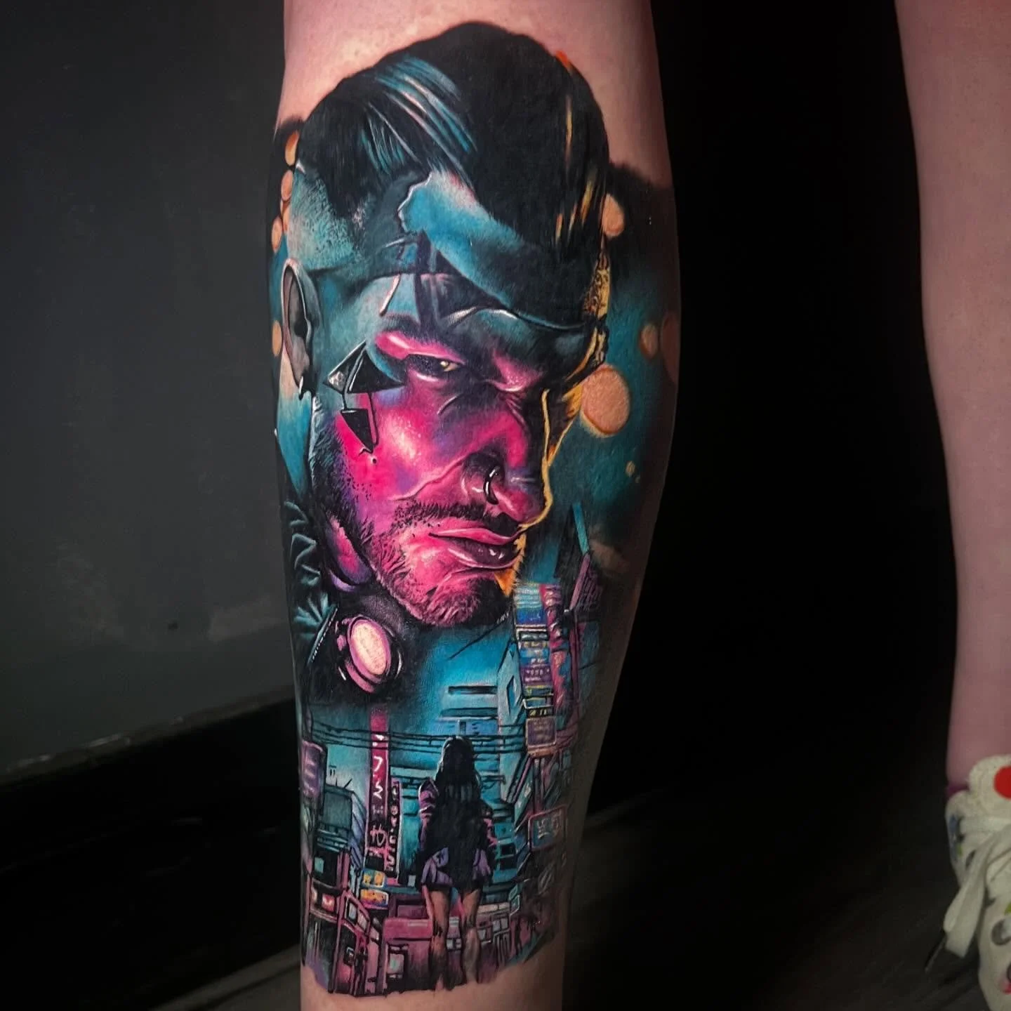Colorful tattoo of a man's face with cityscape at the bottom on a person's leg.