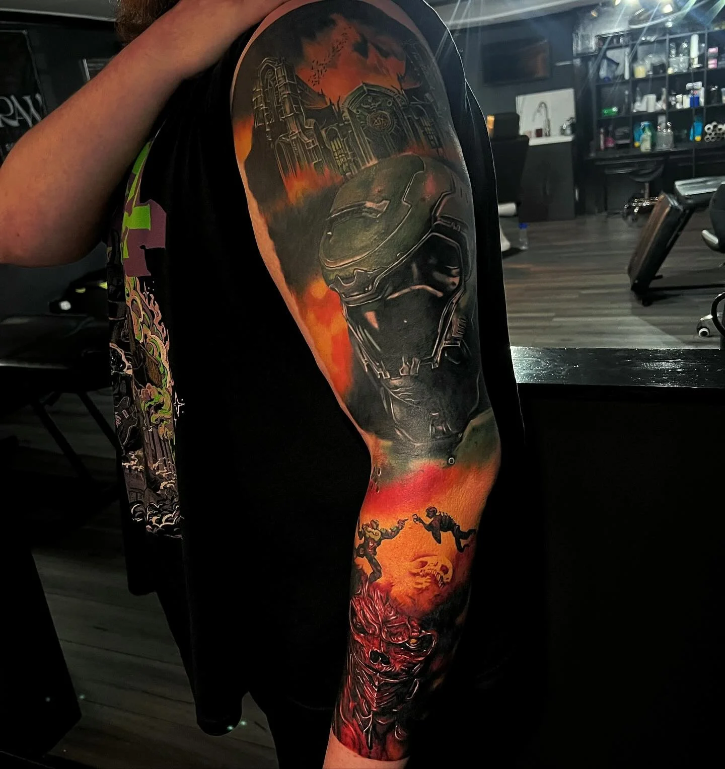 Colorful tattoo of a futuristic soldier wearing a helmet, with a dark background featuring a ruined cityscape and two figures in a fiery landscape.