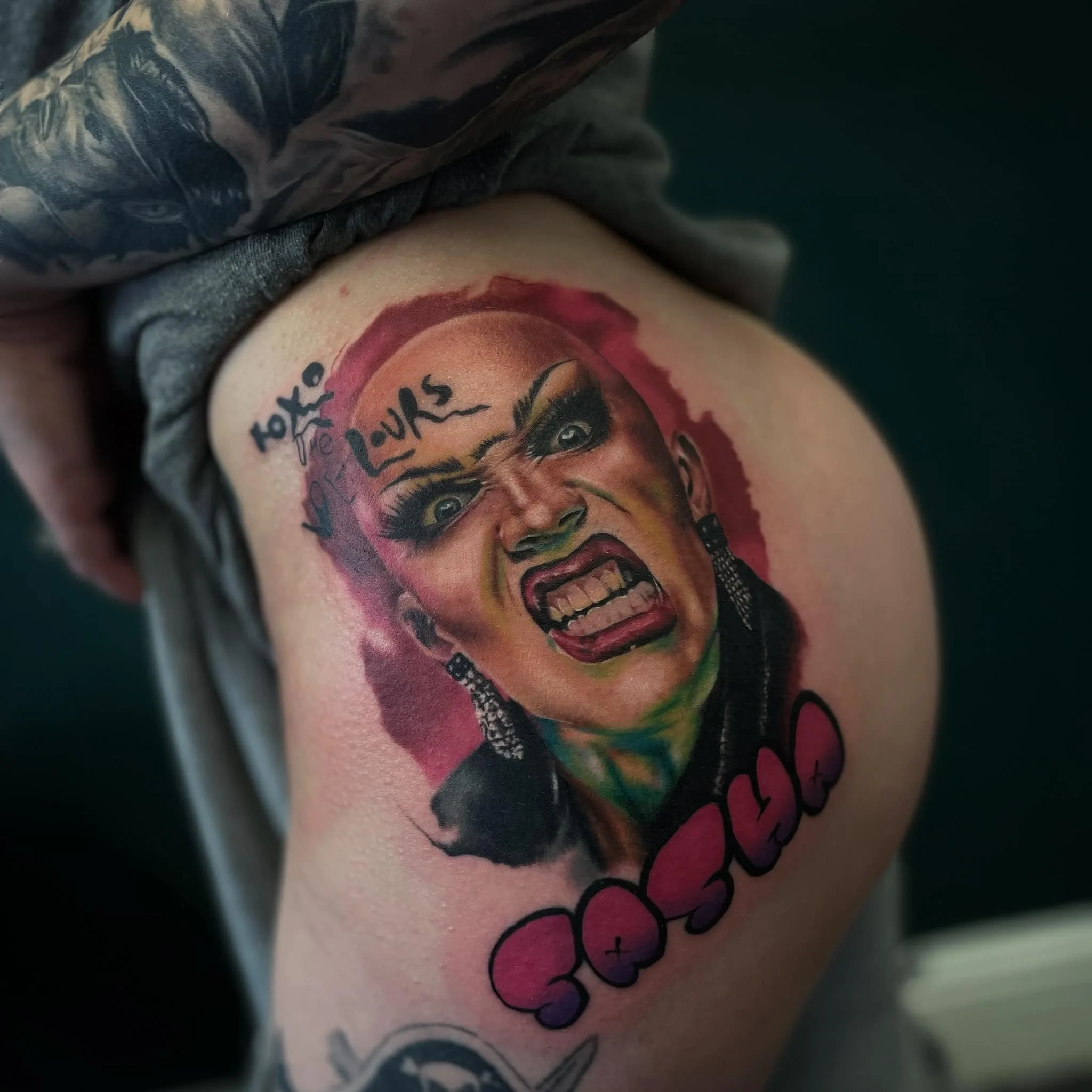 Colorful tattoo of a woman with an angry expression, with words "toxic love" above her face and a pink heart with the word "CASSIE" underneath.