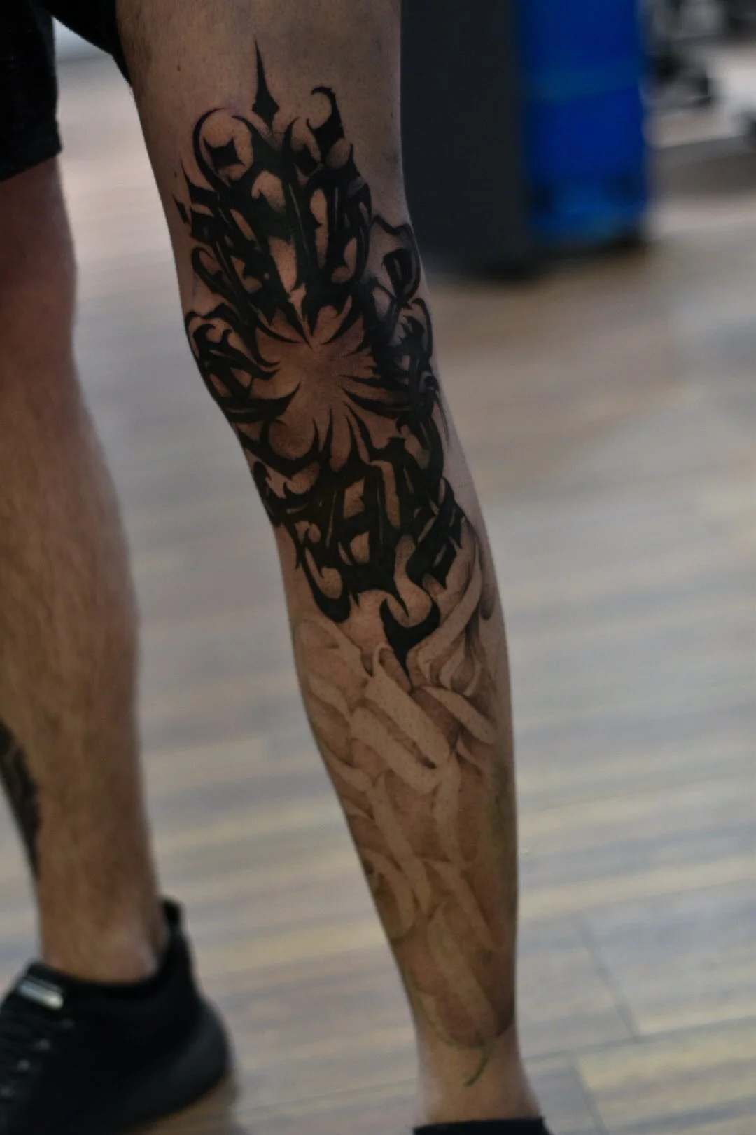 Tattoo of a stylized butterfly or insect with intricate black designs on a person's leg.