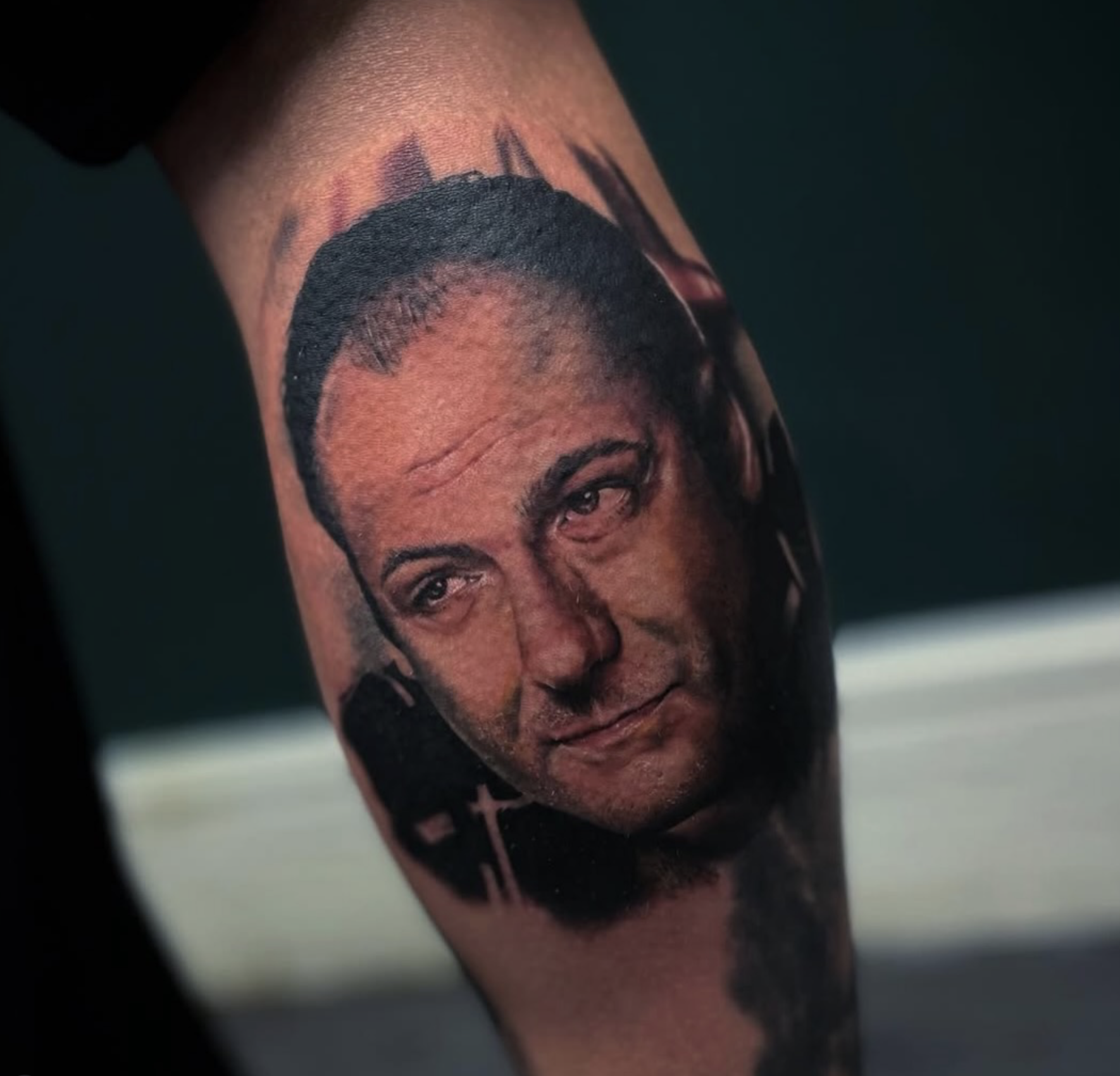 Tattoo of a man's realistic face on someone's arm, including details of his hair, eyes, and expression.