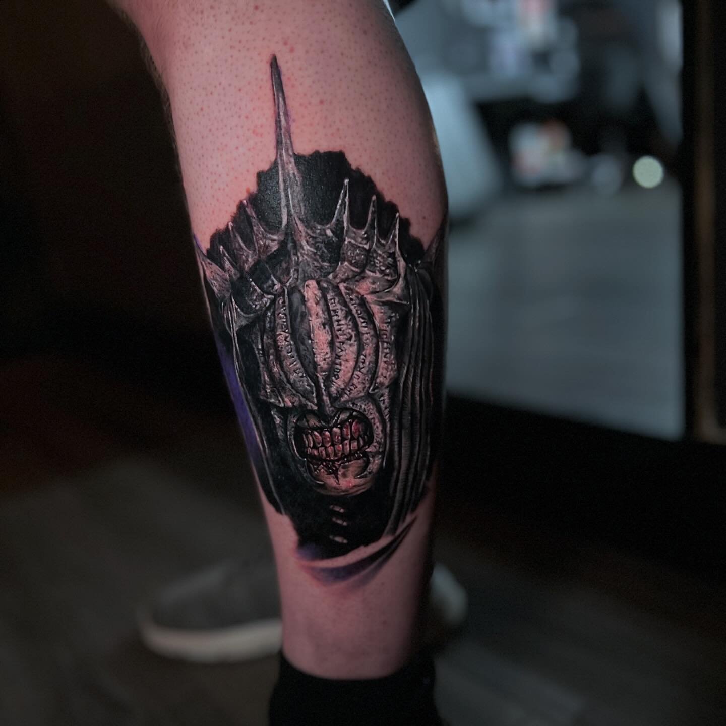 A tattoo of a demonic face with horns, sharp teeth, and menacing eyes with a dark background.