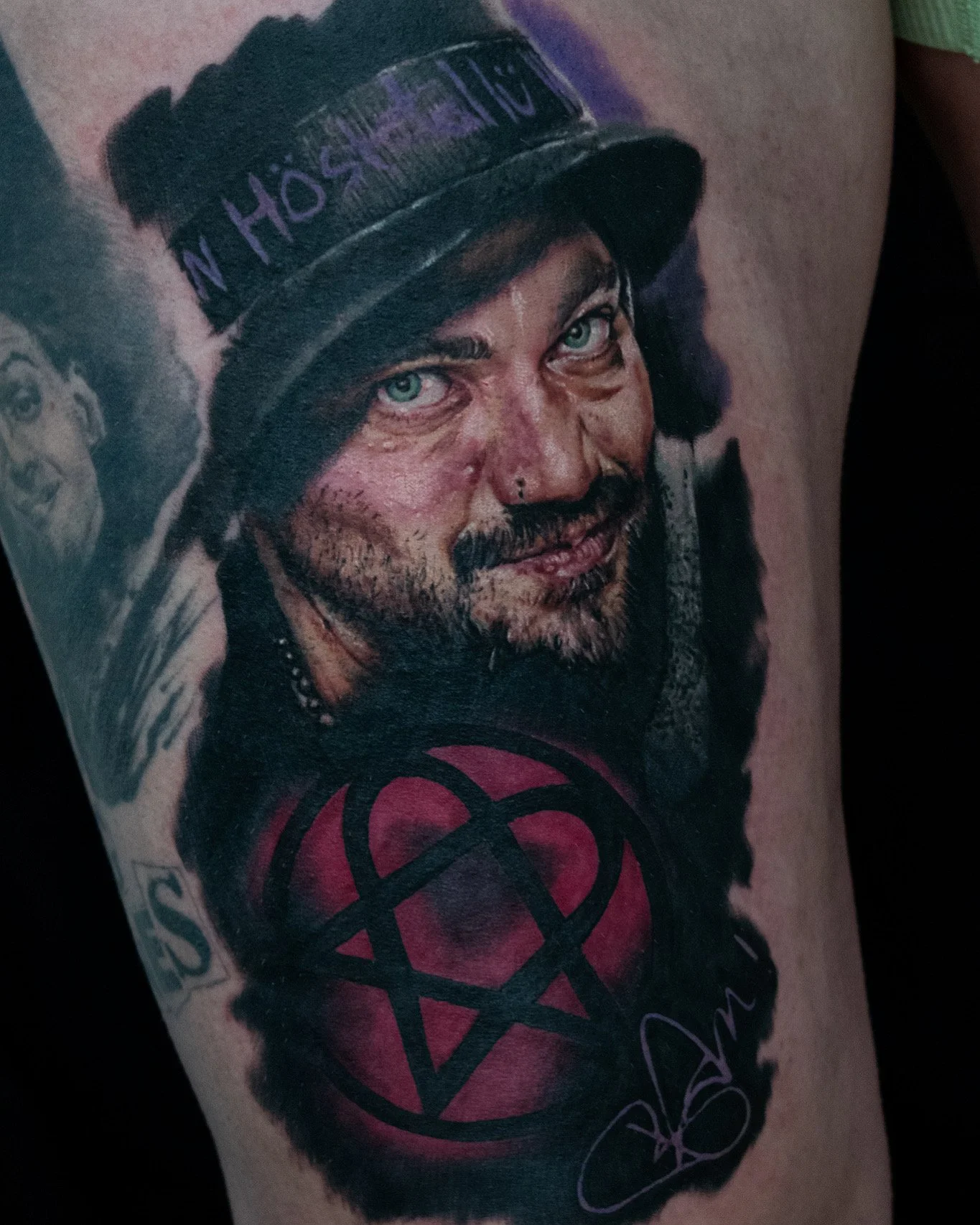 A detailed tattoo of a man's face with blue eyes, a beard, and a nose piercing, wearing a hat with the words "No Hope No Fear" on it, and a pentagram with a red background below his face.