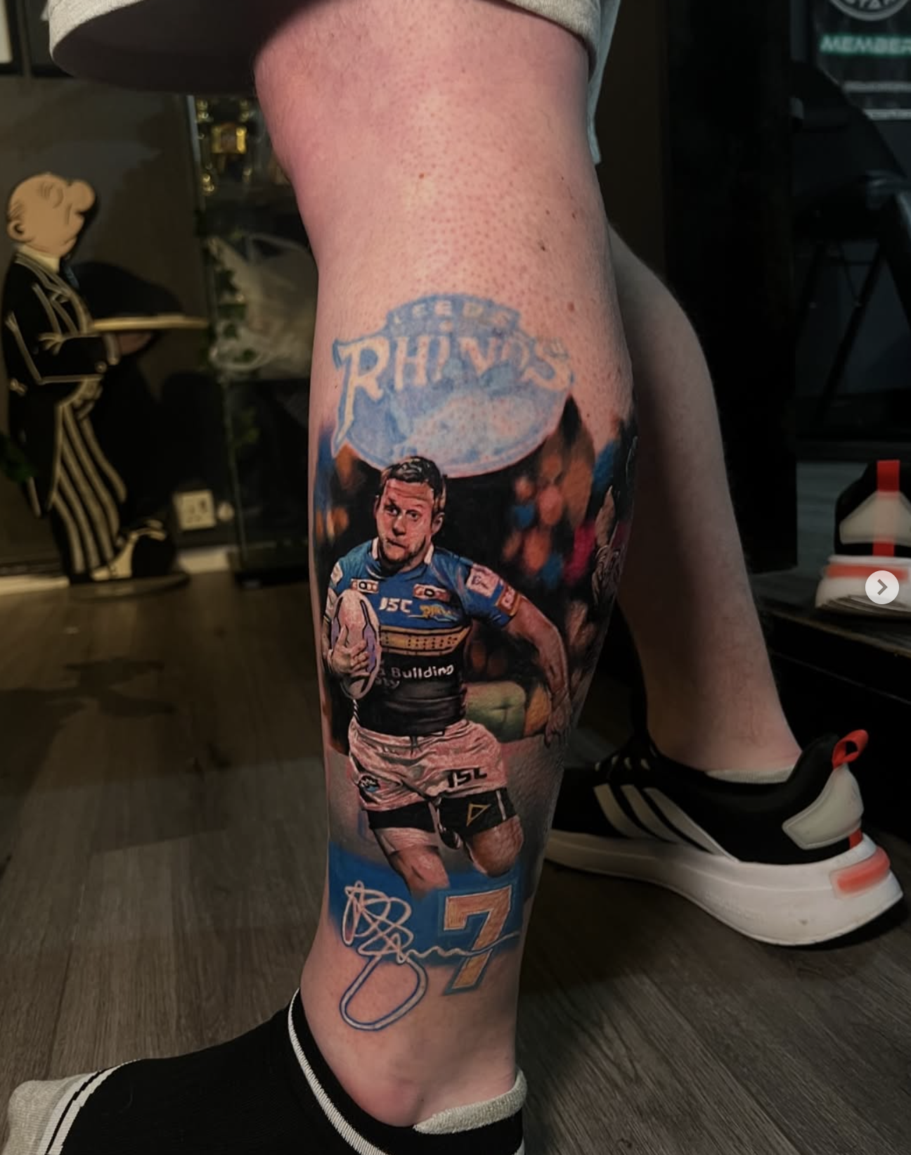 Tattoo of a rugby player holding a rugby ball wearing a uniform with the number 7, with a logo reading 'Reds' above and the number 7 below.