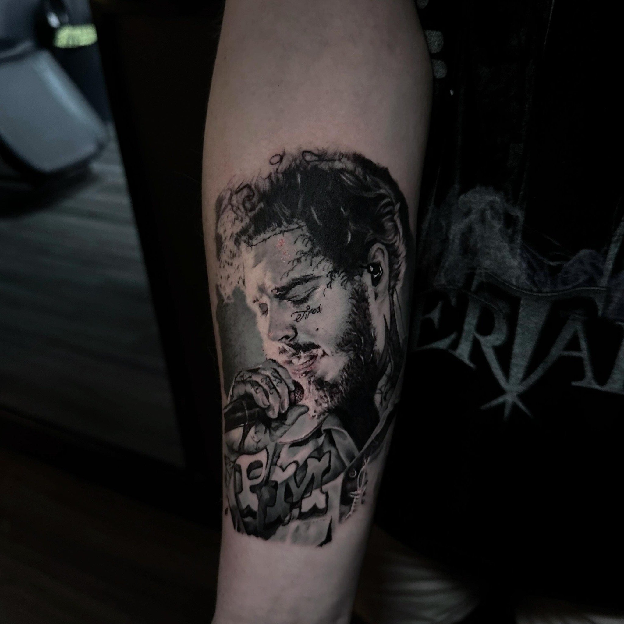 Black and gray tattoo of a man singing with a microphone, winking, with tattoos on his hand and face, and styled hair.