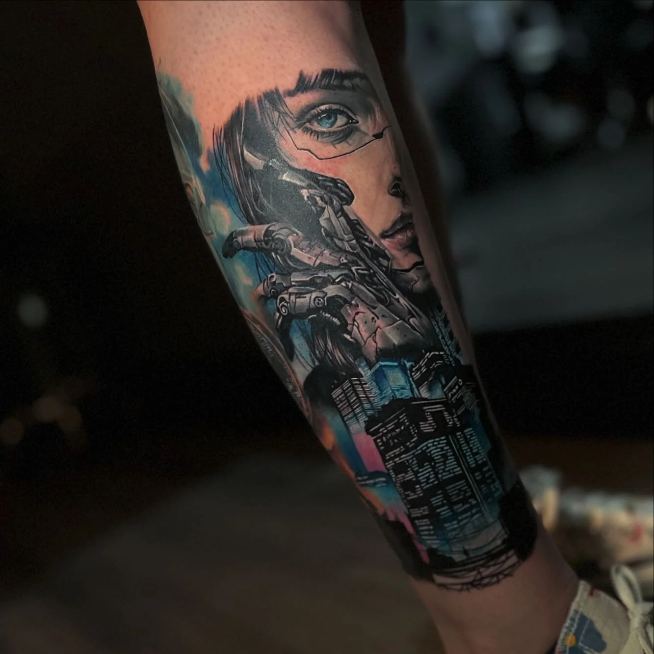 Tattoo of a cybernetic woman with robotic hand, cityscape, and a mix of digital and portrait art on a forearm.