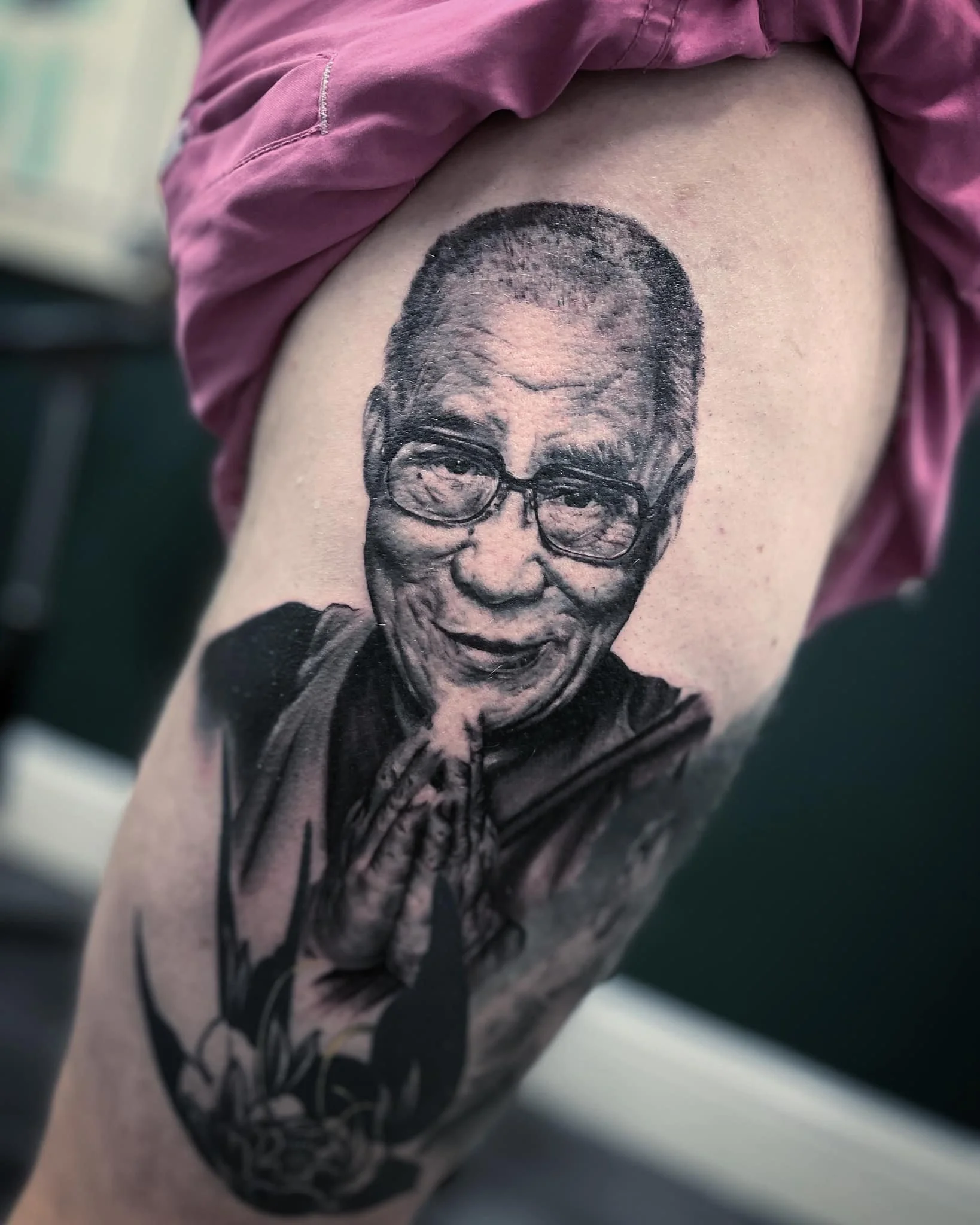 Tattoo of an elderly woman with glasses, smiling with hands in a prayer position.