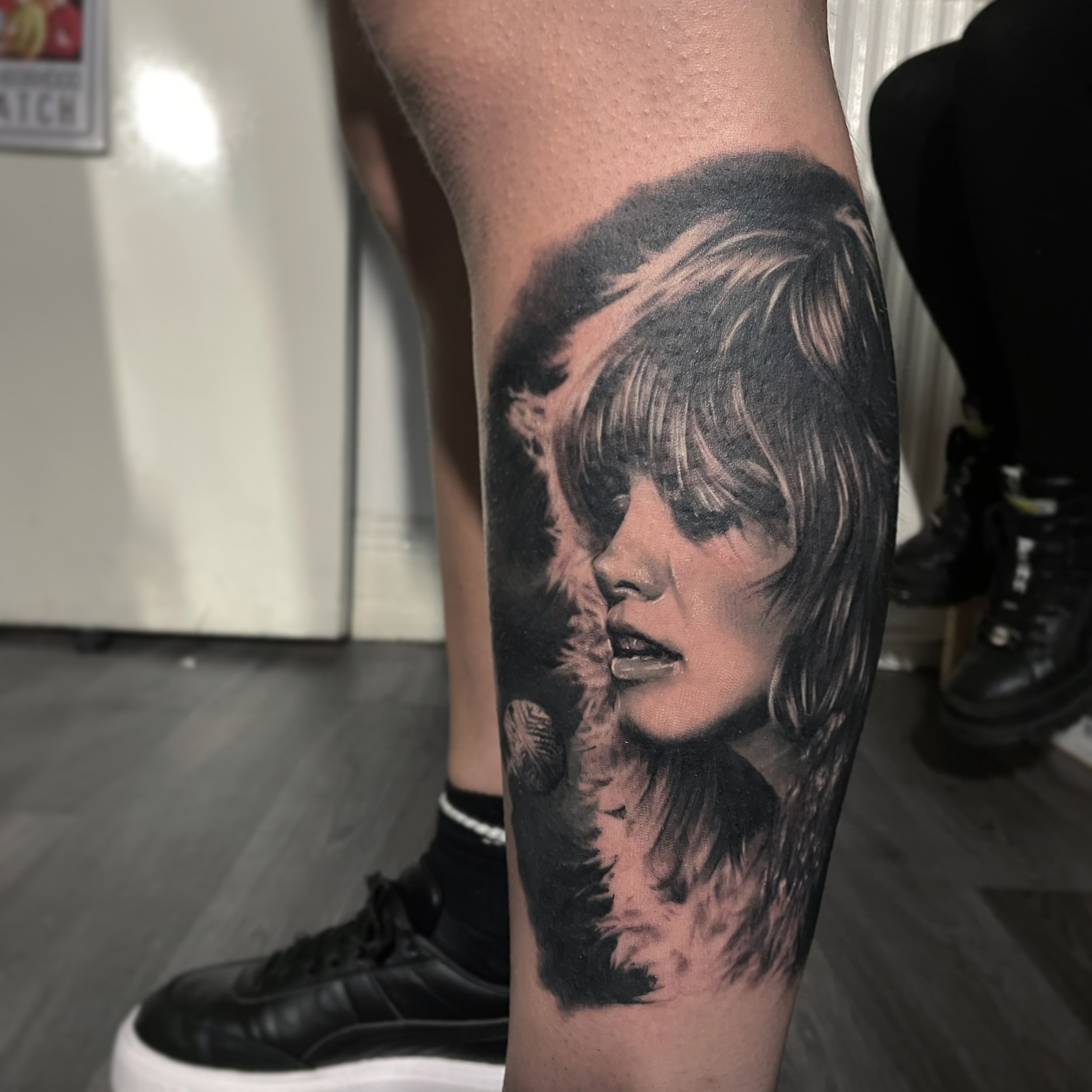 Black and gray tattoo of a woman's face with short, layered hair on a person's leg.