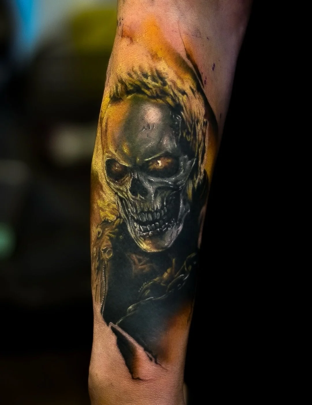 A realistic black and gray tattoo of a skull on a person's arm, with yellow and orange background shading.