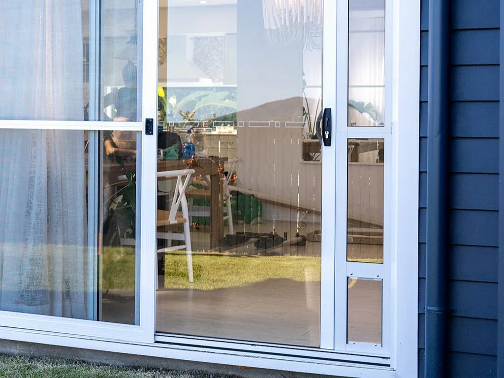 View of a glass sliding door with a pet door panel inserted, with outdoor grass and part of the house exterior.