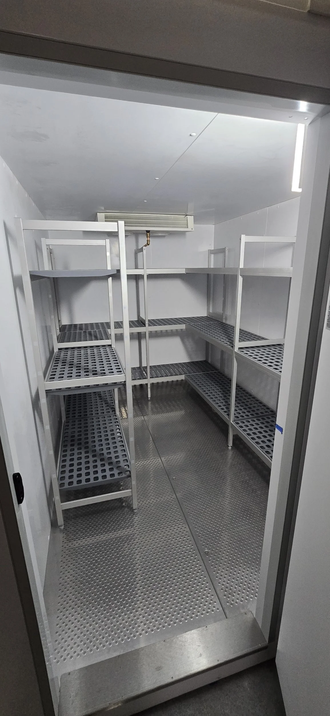 Empty storage cabinet with metallic shelves, grates, and a stainless steel floor, featuring an air vent at the back.
