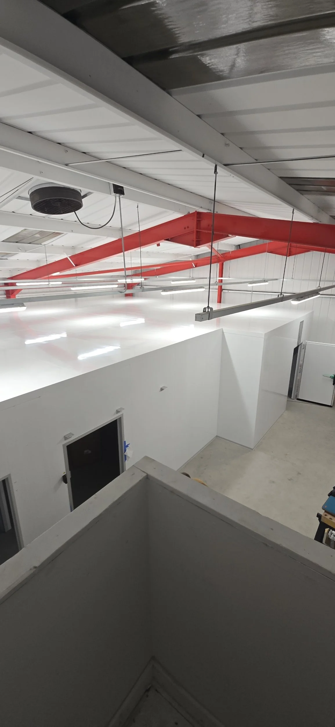 Interior view of a modern industrial or commercial space with white walls, a white ceiling, and exposed red and gray structural beams and piping.