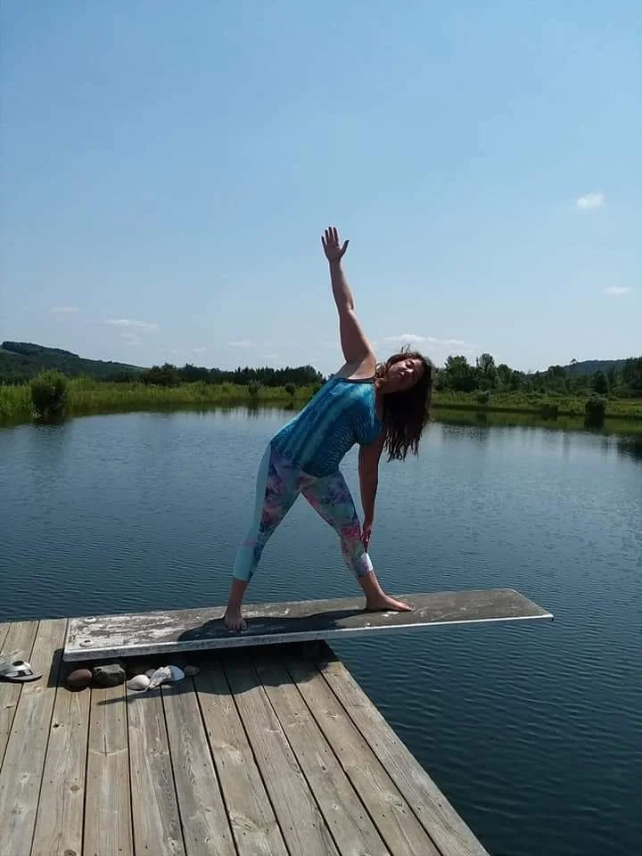 Woman practicing yoga on a dock by a lake on a sunny day.