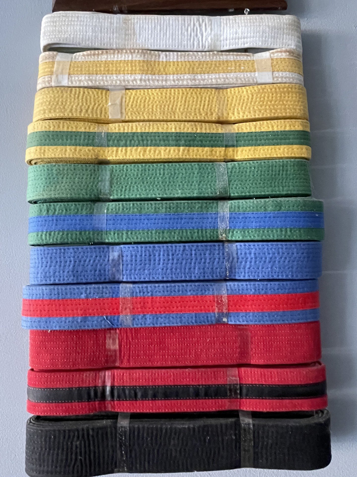 Stacked colorful fabric straps or belts in white, yellow, green, blue, red, and black on a wall-mounted rack.
