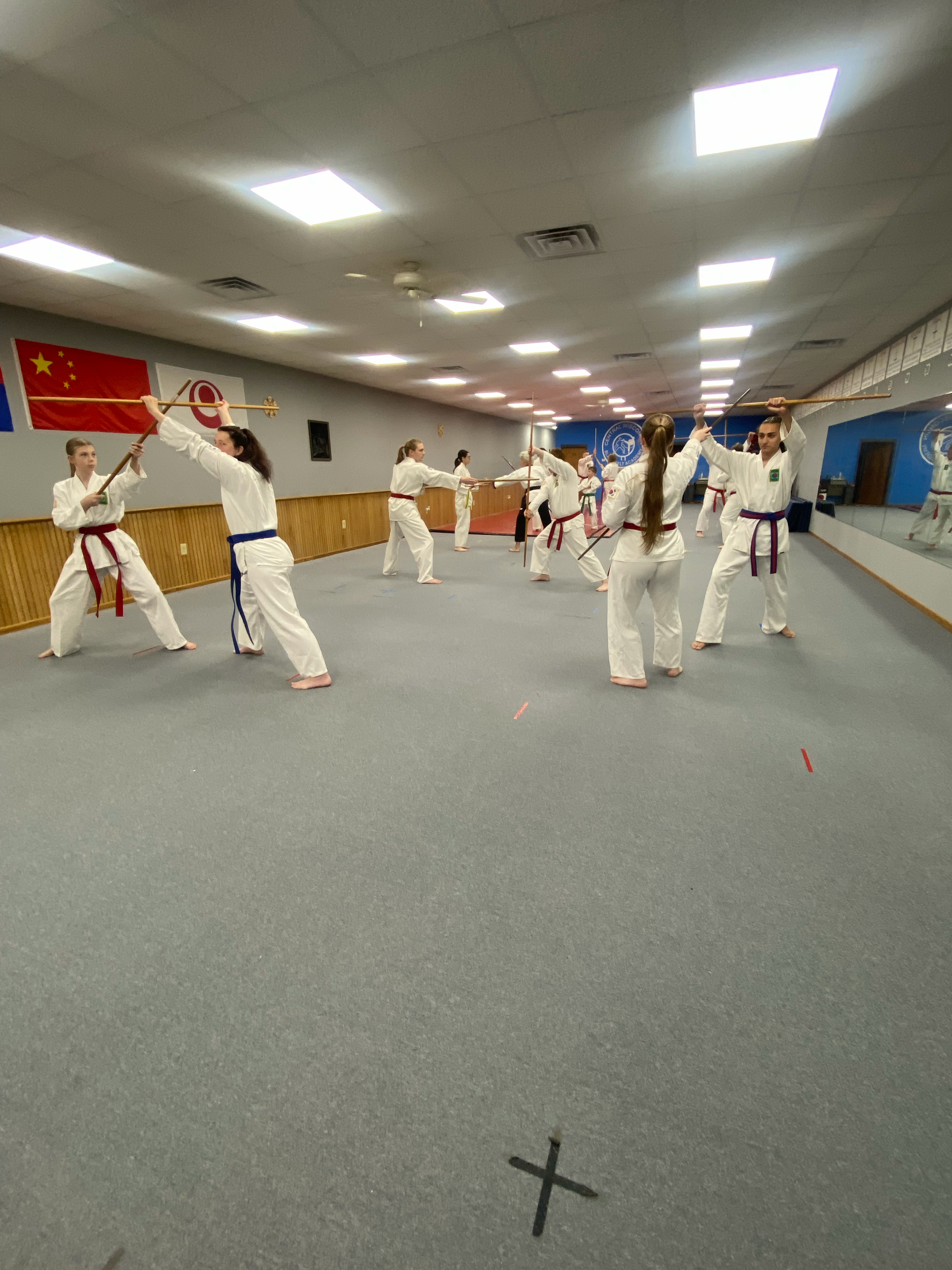 Group of martial artists practicing martial arts in a dojo, with one instructor holding a flag, and a Chinese flag hanging on the wall.