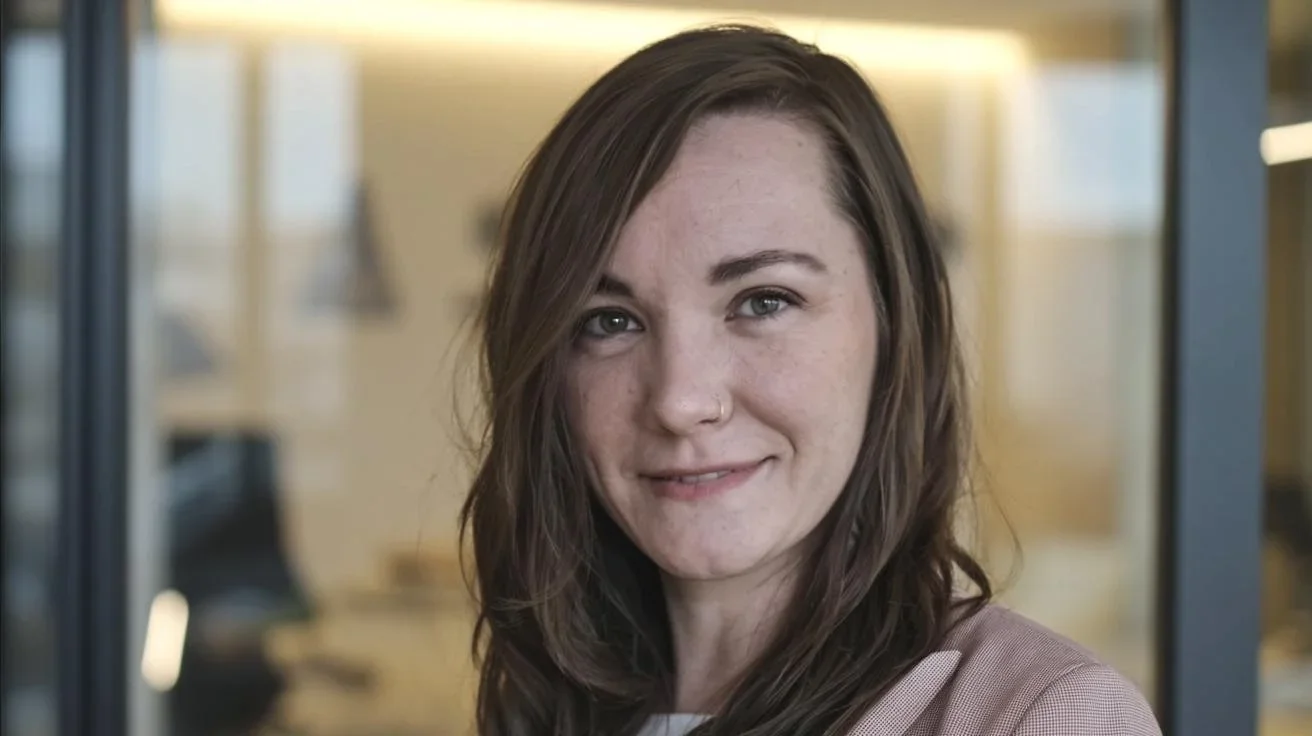 A woman with long brown hair and freckles smiling at the camera, in an indoor setting.