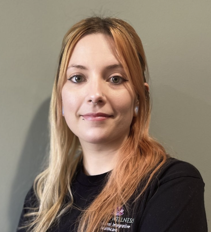 A woman with light skin and long, wavy blonde and reddish hair, wearing a black shirt, standing against a dull green wall.