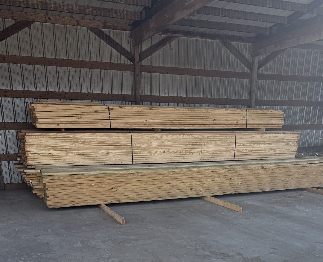 Stacks of wooden planks inside a storage shed with wooden beams and metal wall siding.