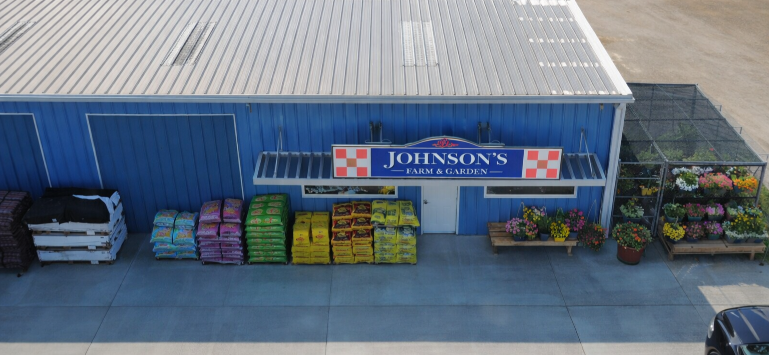 Exterior view of Johnson's Farm & Garden store with garden supplies, flower pots, and garden soil bags displayed outside.