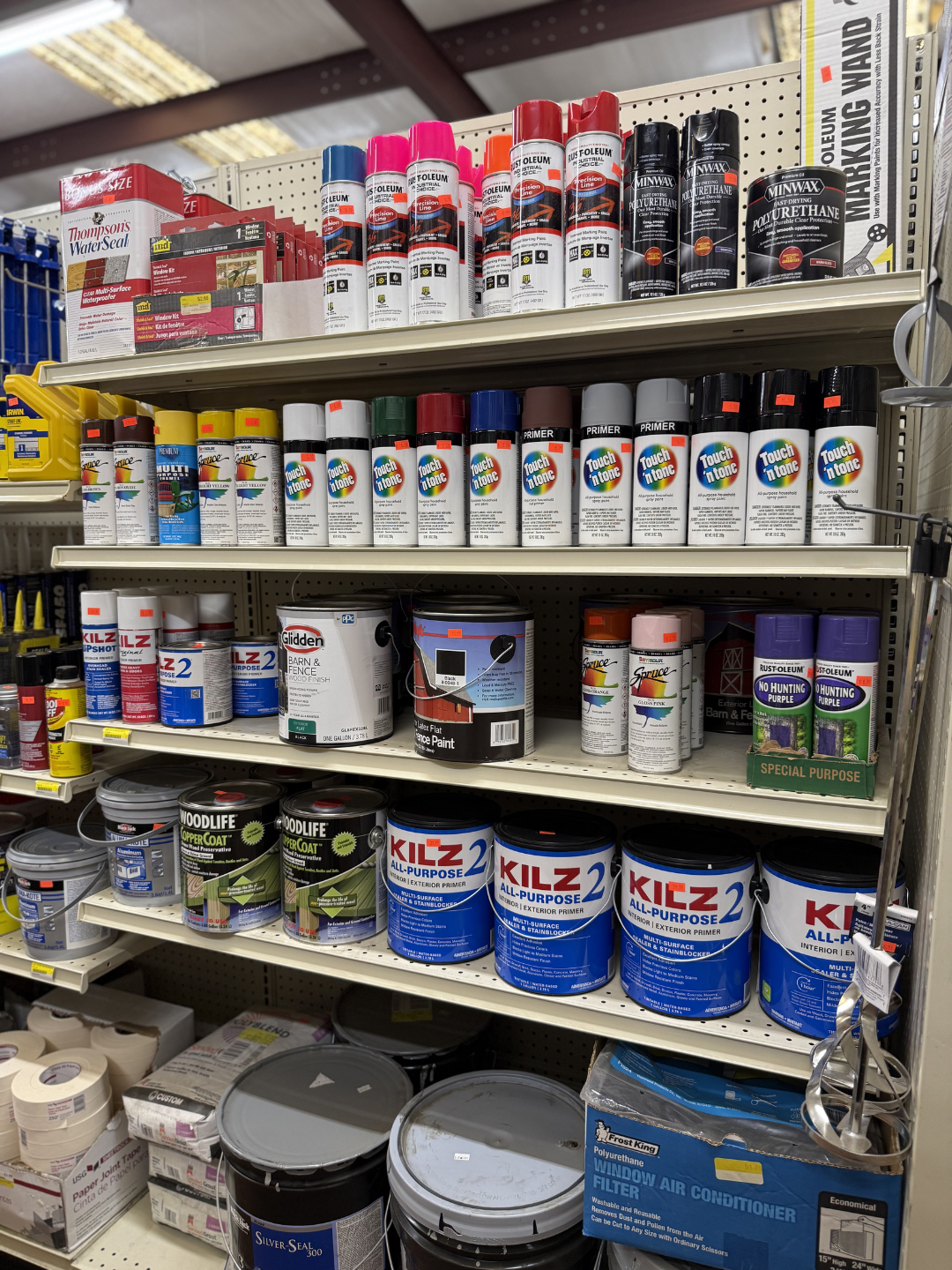 Shelves stocked with cans of spray paint, primer, and paint supplies in a hardware store aisle.