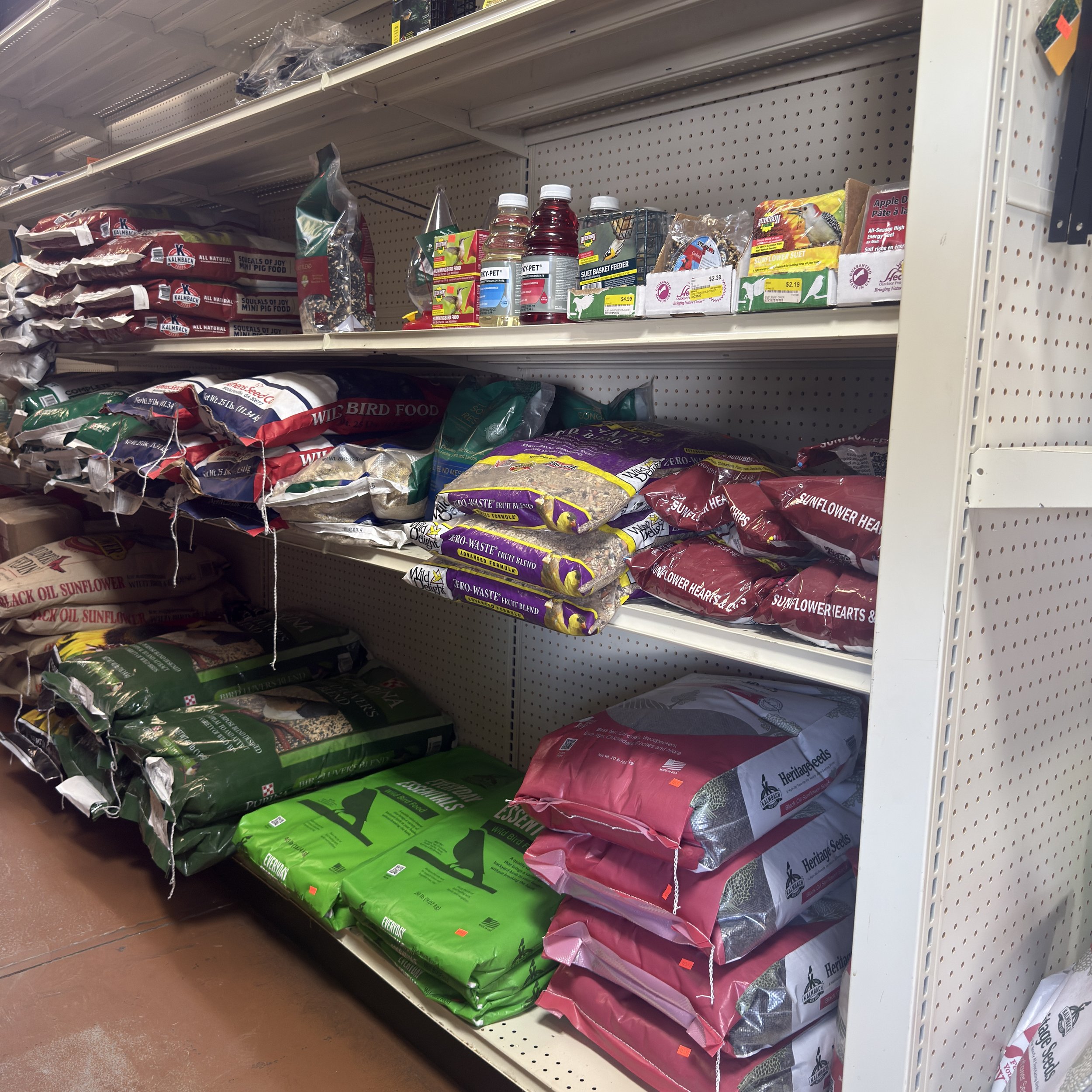 Store shelf stocked with bags of bird seed, small bottles of bird feed, and bird food accessories.