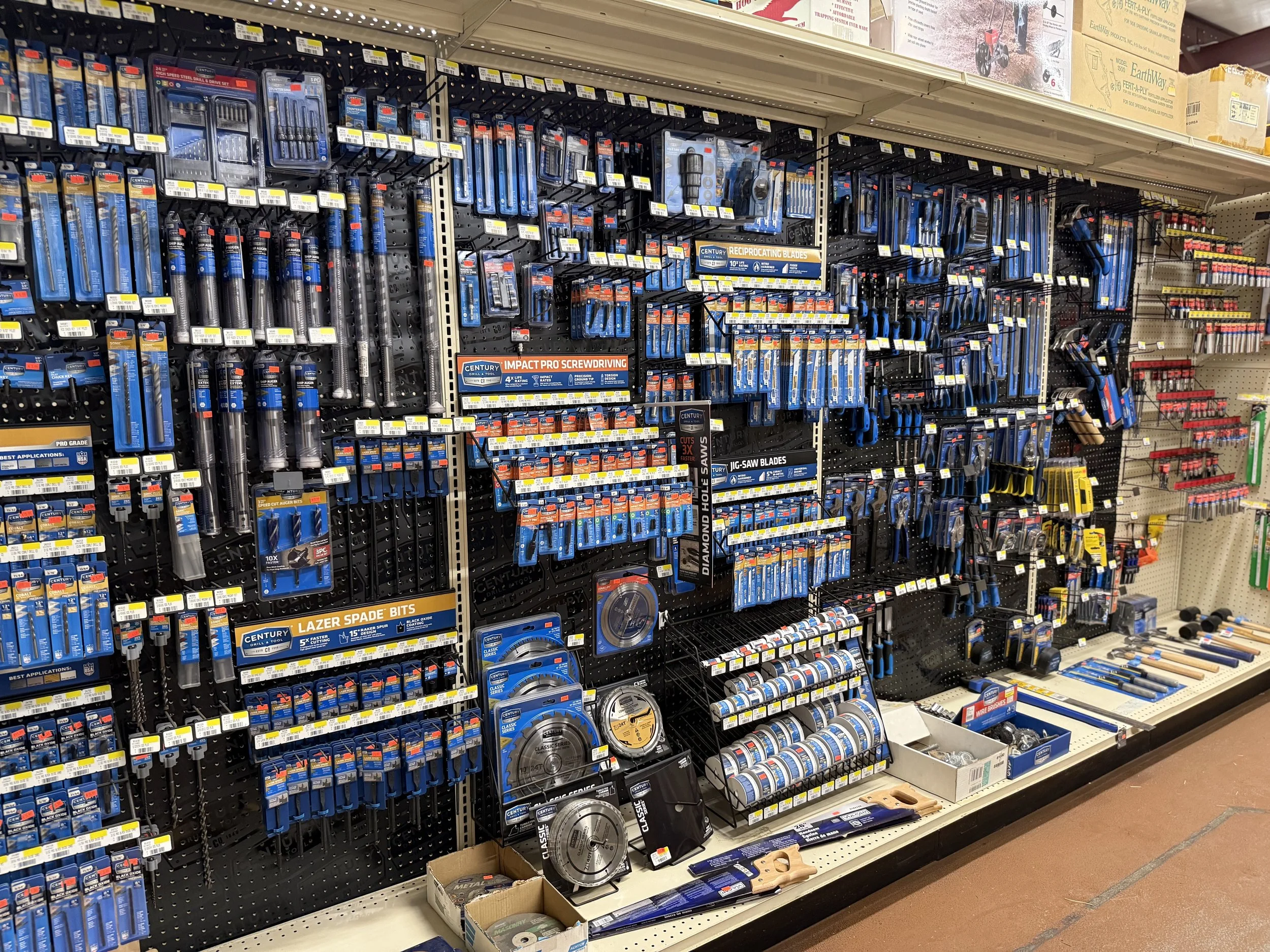 A display of various tools and hardware on store shelves, including screwdrivers, saw blades, and drill bits arranged on black pegboards.