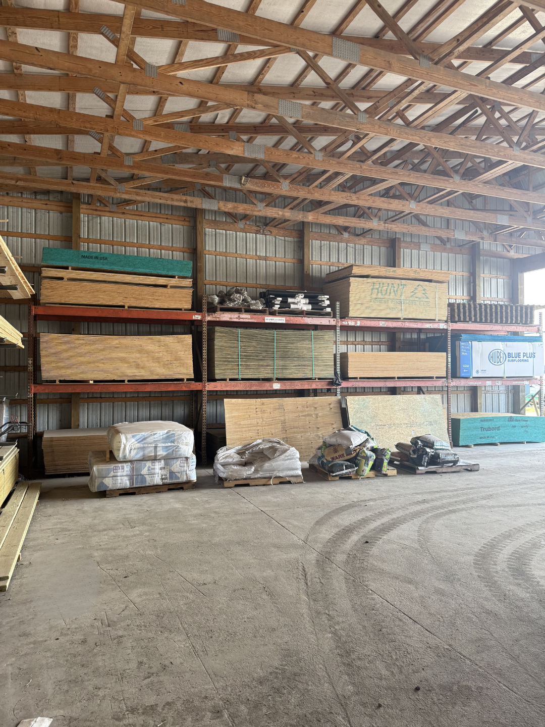 Interior of a hardware store with shelves stocked with lumber, plywood, and construction supplies.