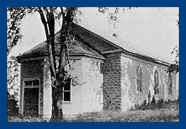 An old, weathered house with a slanted roof, surrounded by trees, in black and white.