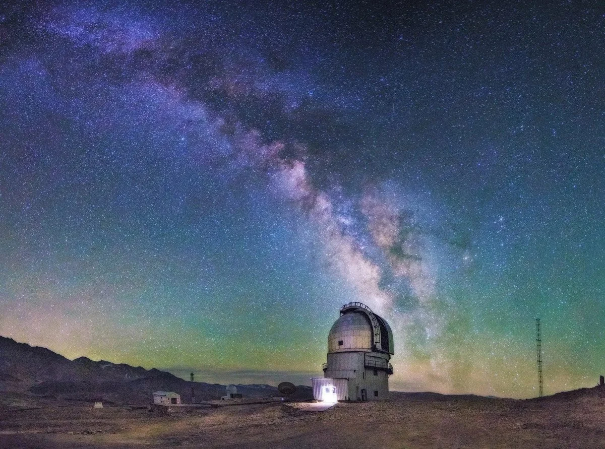 An observatory building under a starry night sky with the Milky Way galaxy visible above.