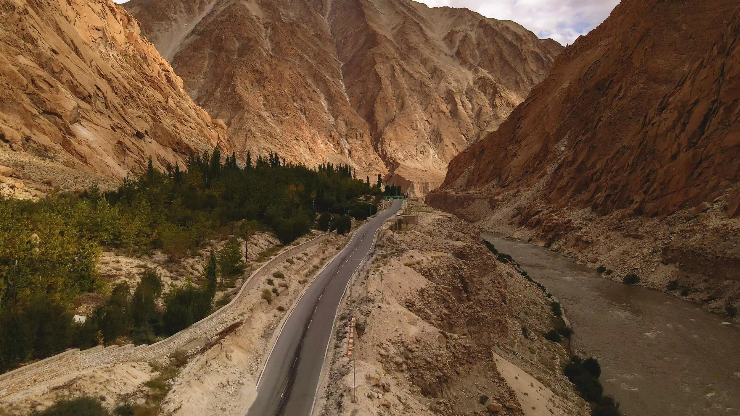 A winding road running through a canyon with steep rocky cliffs on both sides and a river flowing in the canyon below.