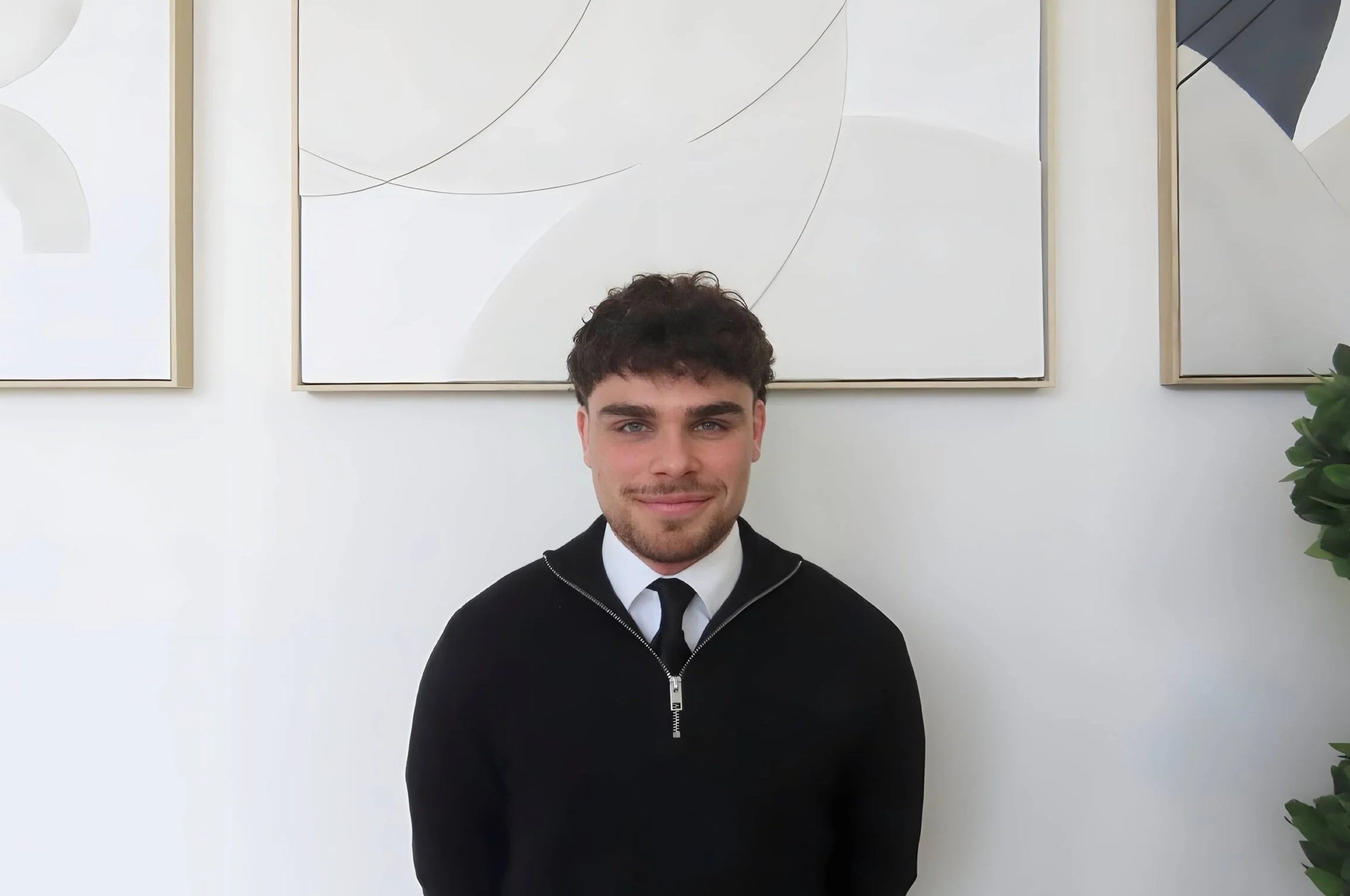 Woman sitting on a bench, writing in a notebook, with abstract artwork resting against the wall beside her in a well-lit room.