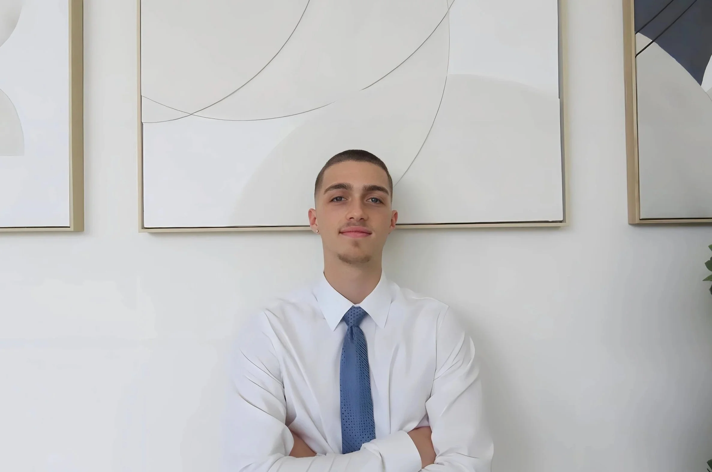 A middle-aged man with gray hair sitting on a beige bench against a plain light-colored wall, looking to the side with a contemplative expression.