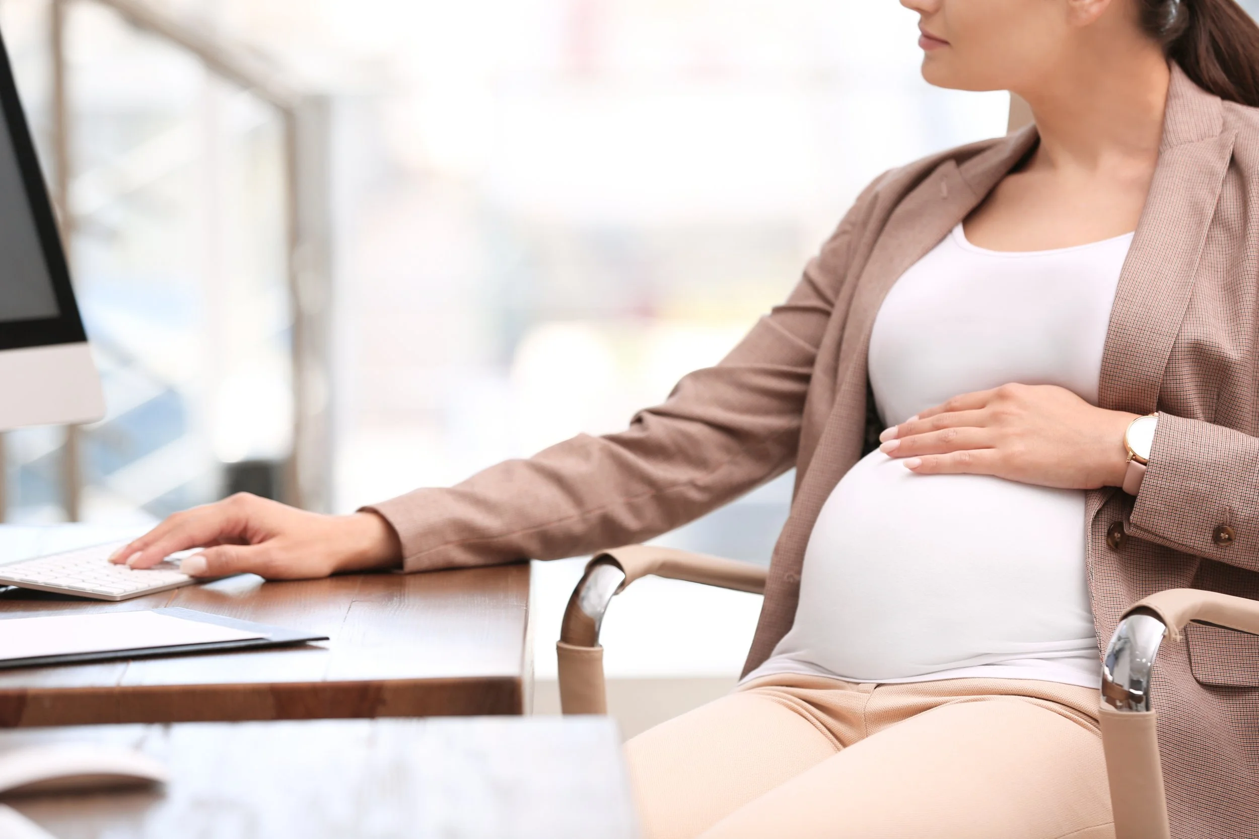 Pregnant woman sitting at a desk using a computer in an office setting.