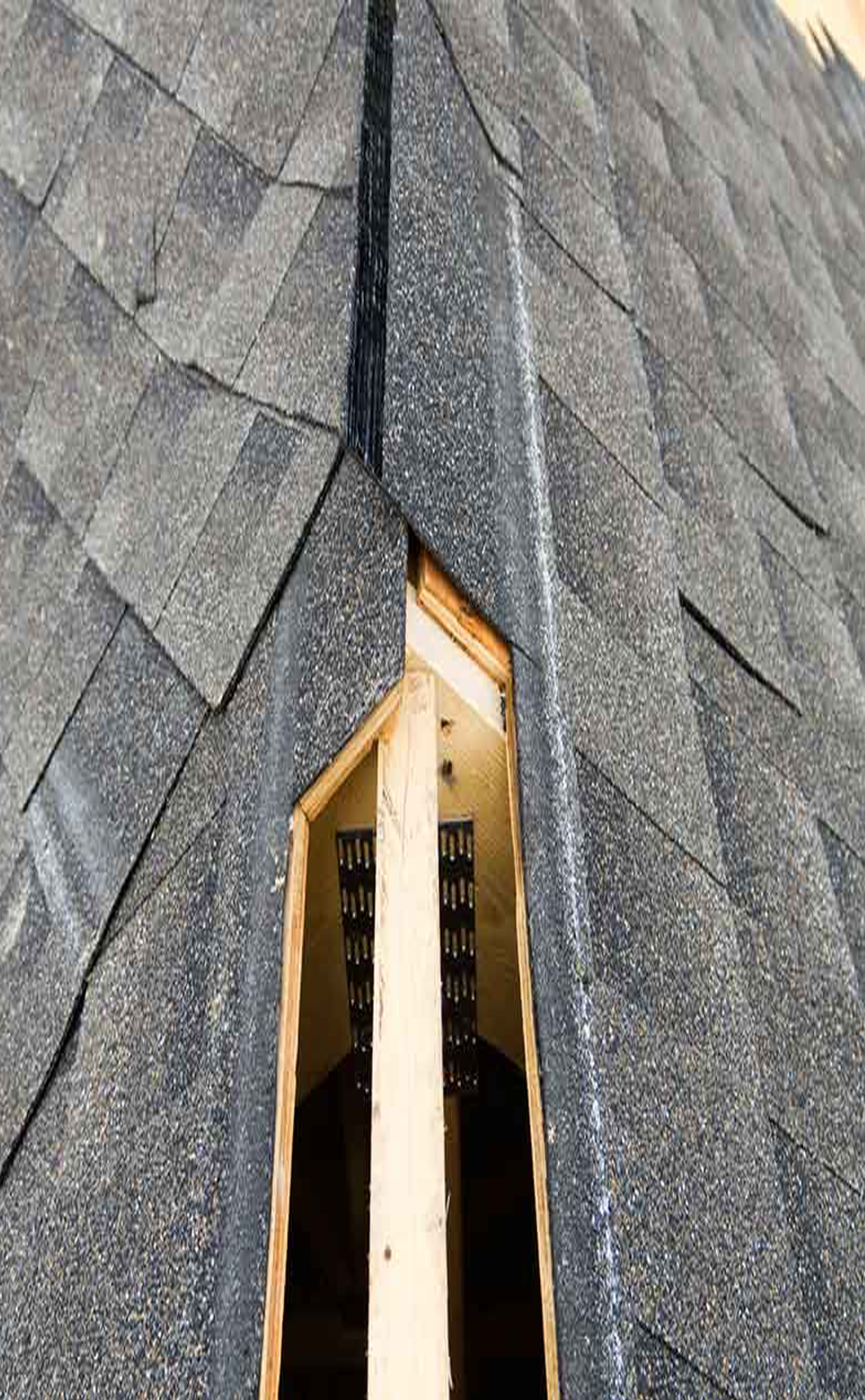 Close-up view of a roof with asphalt shingles, with a section removed to reveal the wooden structure and zippered vent inside.