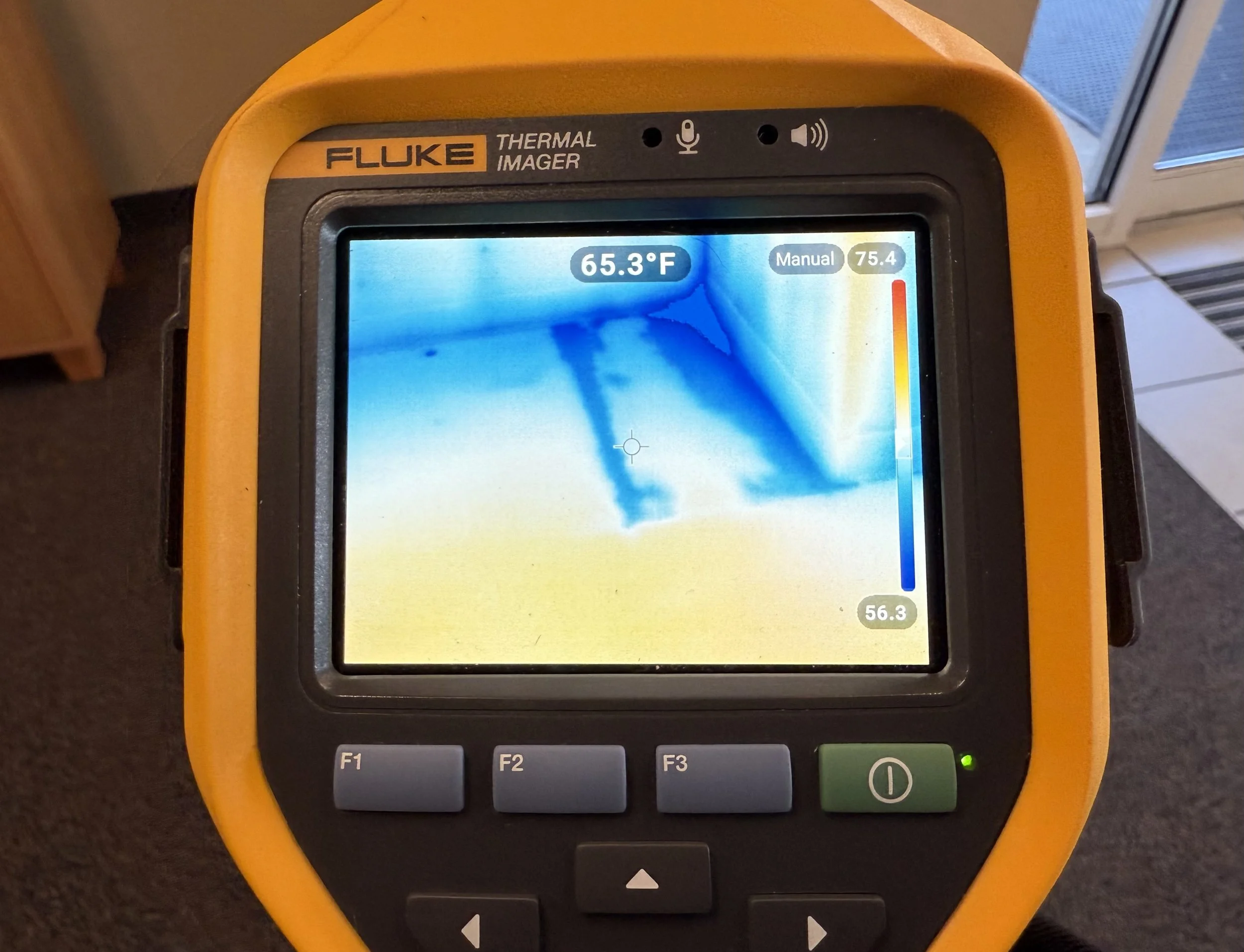 A yellow Fluke thermal imaging camera displaying a thermal image with temperatures of 65.3°F at the top and a color scale ranging from 56.3°F to 75.4°F on the right side. The screen shows a thermal pattern, possibly of a surface or object, in varying shades of blue and yellow.