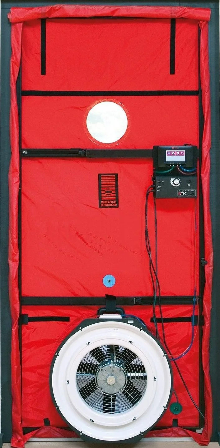A mobile emergency shelter with a red fabric cover, a white circular fan at the bottom, a small round window above the fan, and a control panel with a digital screen on the right side.