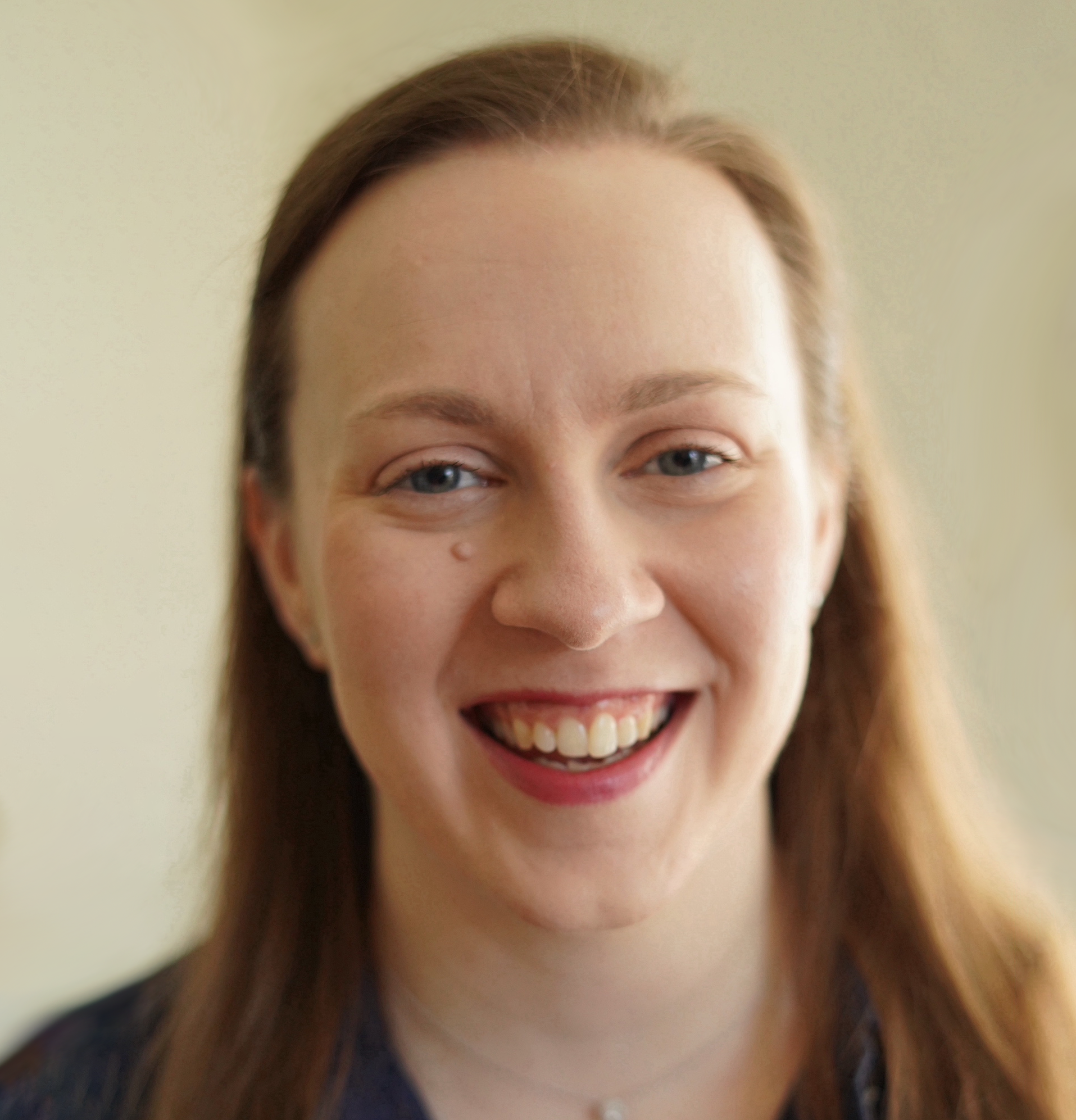 Close-up of a woman with light brown hair smiling in front of a light background.