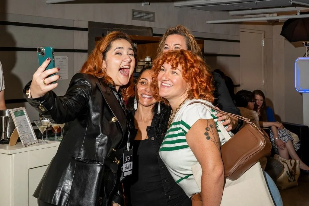 Four women taking a selfie at a social event, smiling and posing together indoors.