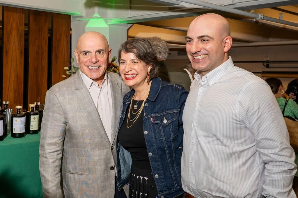 Three people smiling and posing together at an event, with bottles on a table behind them.