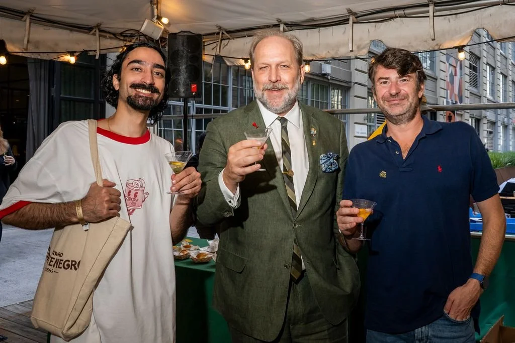Three men standing together at an outdoor event, holding drinks and smiling at the camera.